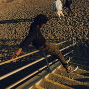 Men's Hawthorne Slip On in Pavement suede, worn by a person leaping on beach stairs at dusk