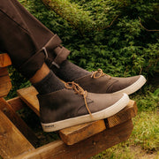 Men's Maslon Desert Boot in Charcoal leather, close-up worn with dark pants on wooden pallets