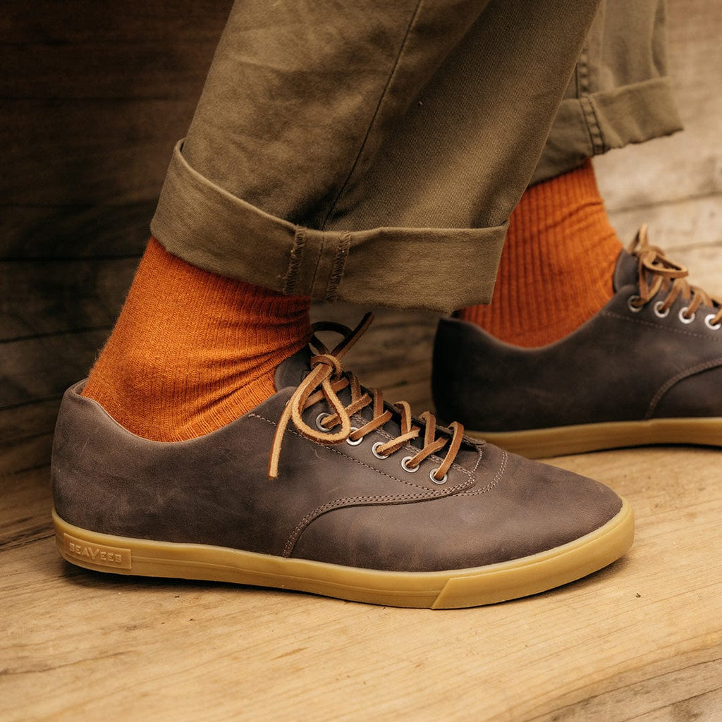 Men's Hermosa Sneaker in Charcoal leather, close-up worn with orange socks and olive pants on a wood surface