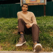Men's Maslon Desert Boot in Charcoal leather, worn with brown pants by a person seated on grass