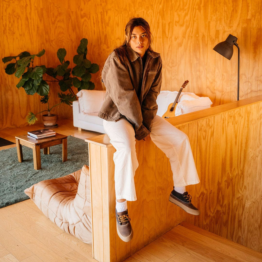 Women's Carson 3 Eye Boot in Peacoat Navy/Bark leather, worn by a person seated on a wooden counter