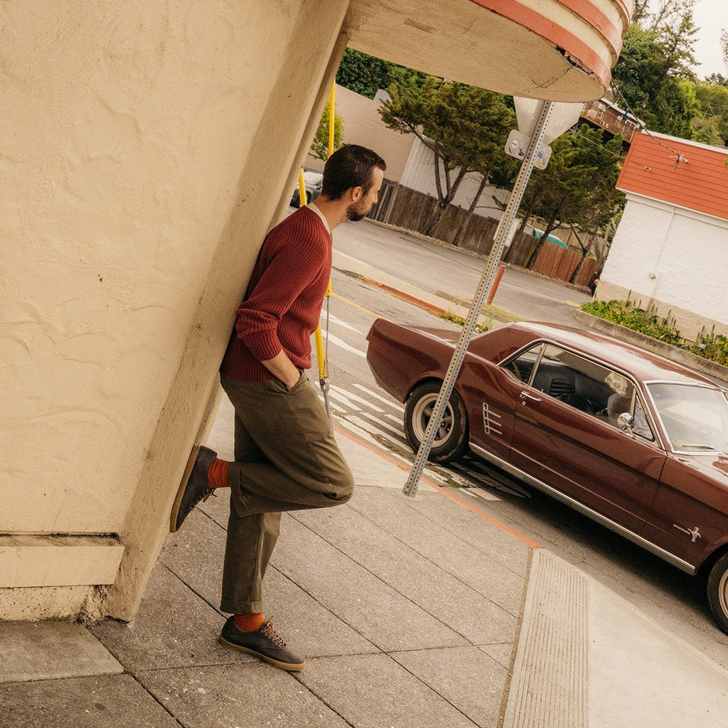 Men's Hermosa Sneaker in Charcoal leather, worn by a person leaning on a building beside a vintage car