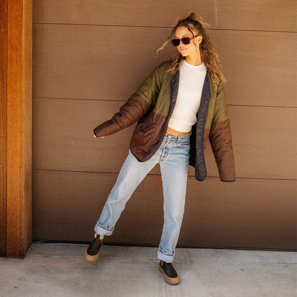 Women's Ballard Boot in Coffee Bean leather, worn by a person standing against a brown wall in a green jacket