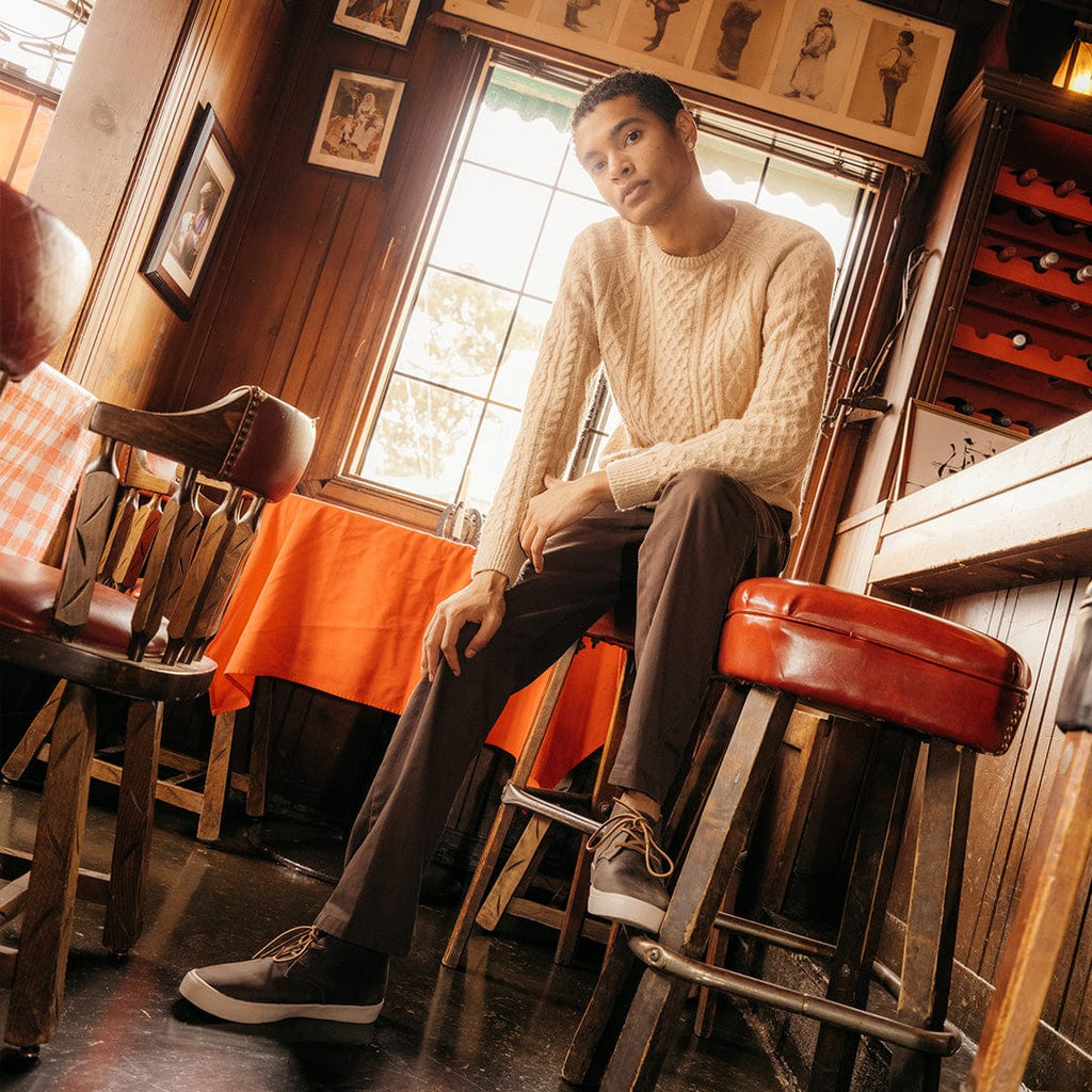 Men's Maslon Desert Boot in Charcoal leather, worn with brown pants by a person seated on a bar stool