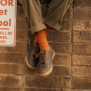 Men's Hermosa Sneaker in Charcoal leather, close-up worn with orange socks against a brick wall