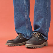 Men's Larkspur Lug Boat Shoe in Dark Chocolate leather, worn with wide-leg jeans on a coral background, close up