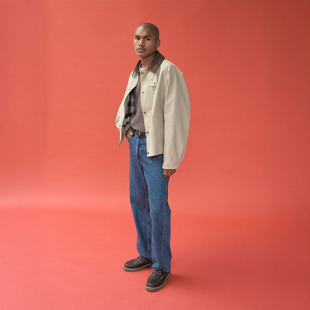 Men's Larkspur Lug Boat Shoe in Dark Chocolate leather, worn by a person standing on a coral background in a light jacket