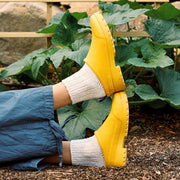 Women's Bodega Clog in Calendula rubber, worn with white socks and wide-leg jeans in a garden, soles up