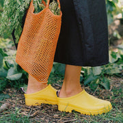 Women's Bodega Clog in Calendula rubber, worn with black pants, carrying an orange mesh bag