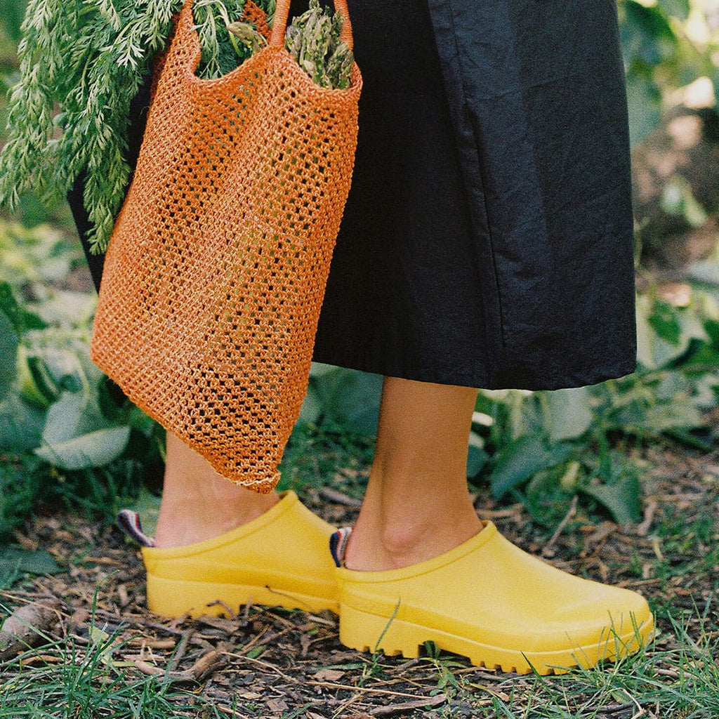 Women's Bodega Clog in Calendula rubber, worn with black pants, carrying an orange mesh bag