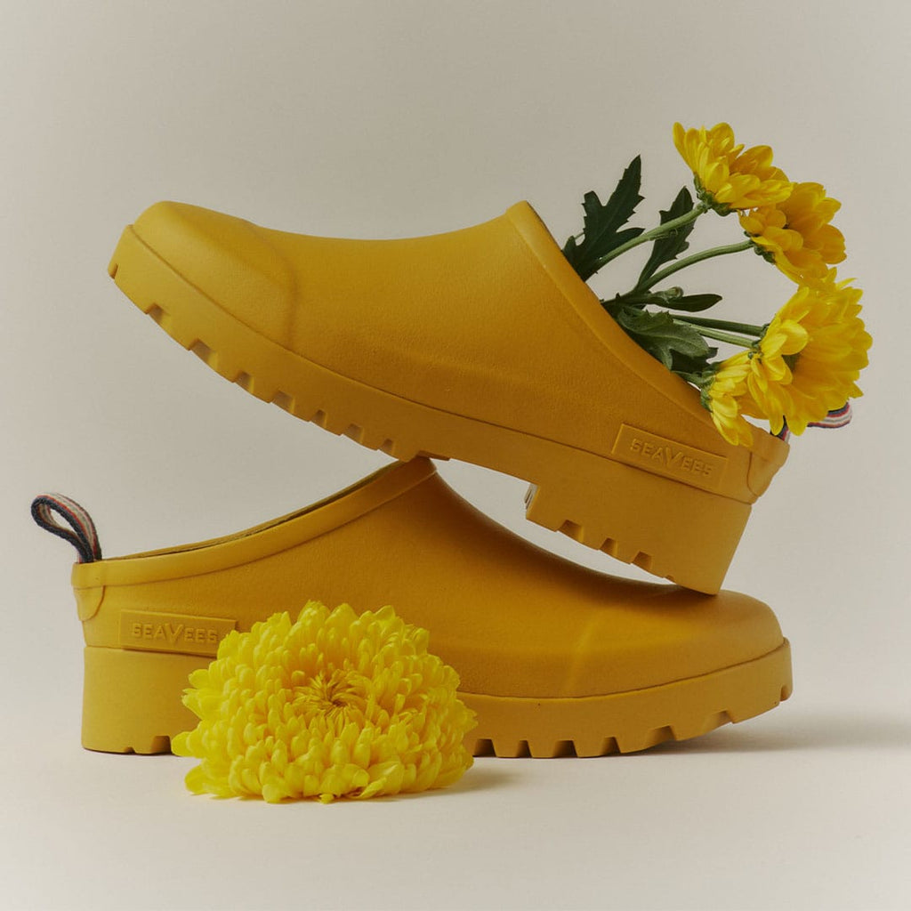 Women's Bodega Clog in Calendula rubber, pair with yellow flowers tucked inside on a tan background
