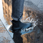 Women's Bolinas Off Shore Boot in Black rubber, close-up of a foot splashing through a puddle