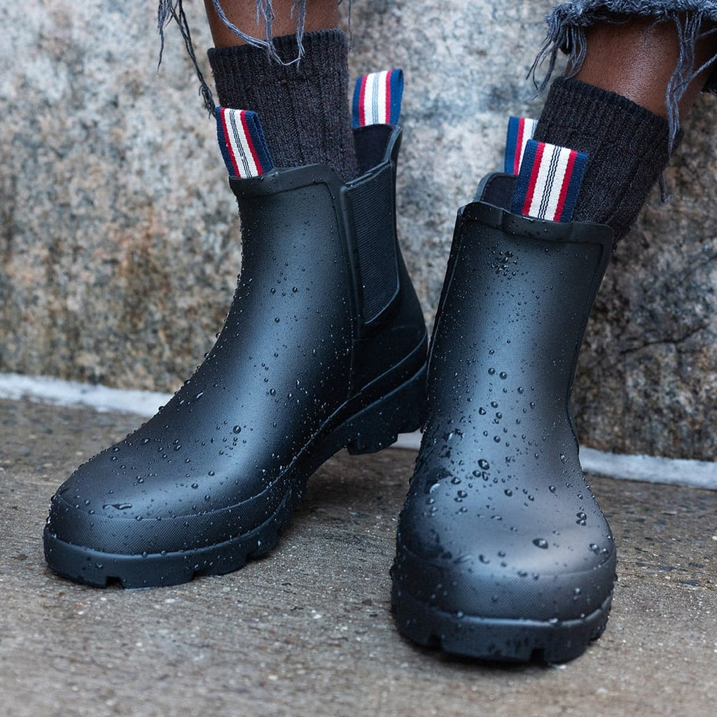 Women's Bolinas Off Shore Boot in Black rubber, close-up of both boots wet with rain, worn with striped socks