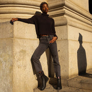 Women's Bolinas Off Shore Boot in Black rubber, worn with dark pants by a person leaning on a stone column