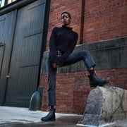 Women's Bolinas Off Shore Boot in Black rubber, worn with dark jeans by a person stepping up on a stone block