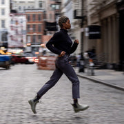 Women's Bolinas Off Shore Boot in Military Olive rubber, worn by a person running down a cobblestone city street