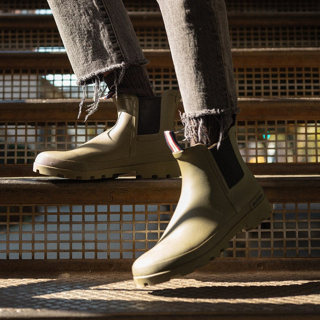 Women's Bolinas Off Shore Boot in Military Olive rubber, close-up worn with gray pants on metal steps