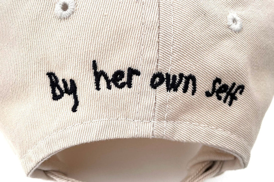 Close up of black embroidered By Her Own Self text under the khaki hat brim