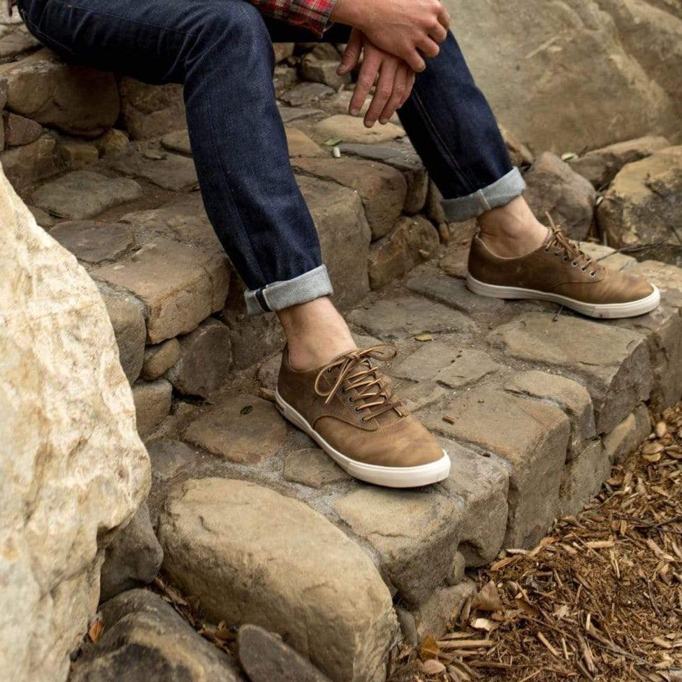 Men's Hermosa Sneaker in Elmwood leather, worn with dark jeans on stone steps
