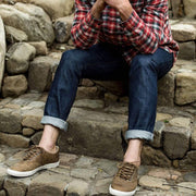 Men's Hermosa Sneaker in Elmwood leather, worn with cuffed jeans by a person seated on stone steps