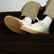 Men's Diamond Cup sneaker in Black leather, ecru pair worn with khaki pants, sole raised on a brown sofa