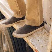 Men's Hawthorne Slip On in Elmwood leather, close-up worn with khaki pants on a wooden ledge