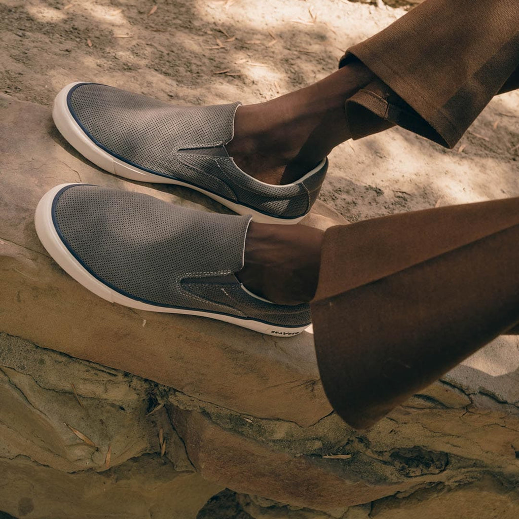 Men's Hawthorne Slip On in Pavement suede, close-up of both shoes worn with brown pants on rocks