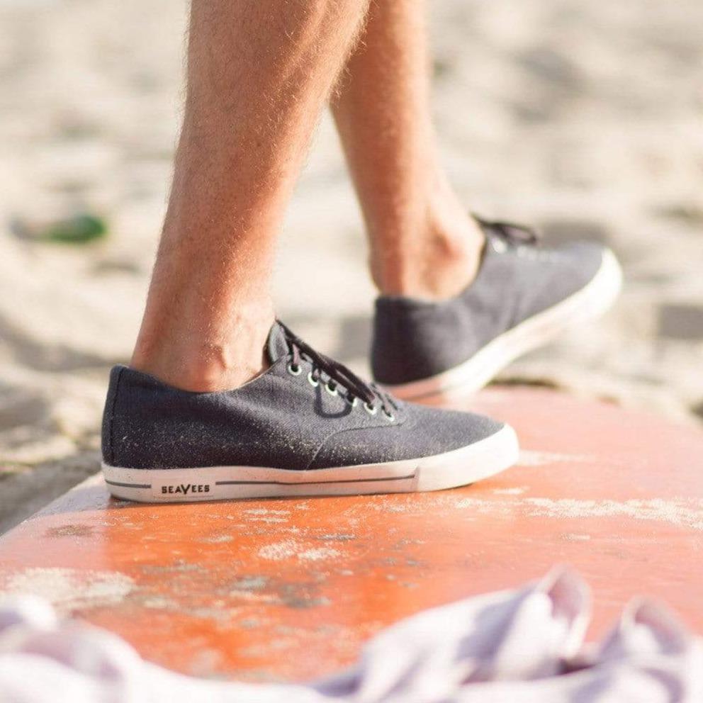 Men's Hermosa Sneaker in Slate Navy canvas, close-up worn on a weathered orange surface by the beach