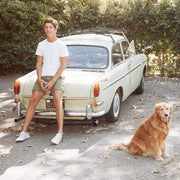 Men's Hermosa Sneaker in Natural canvas, worn with shorts by a person seated on a vintage car bumper beside a dog