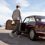 Men's Huntington Middie sneaker in Oyster suede, worn with khaki pants by a person stepping out of a vintage car
