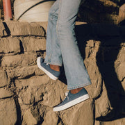 Men's Legend Sneaker in True Navy canvas, worn with light jeans on rocky steps