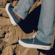 Men's Legend Sneaker in True Navy canvas, close-up worn with light jeans on a rock wall