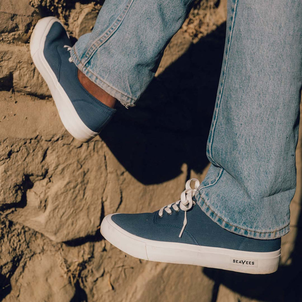 Men's Legend Sneaker in True Navy canvas, close-up worn with light jeans on a rock wall