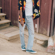 Men's Legend Sneaker in True Navy canvas, worn with light jeans and a floral shirt outside a wooden building
