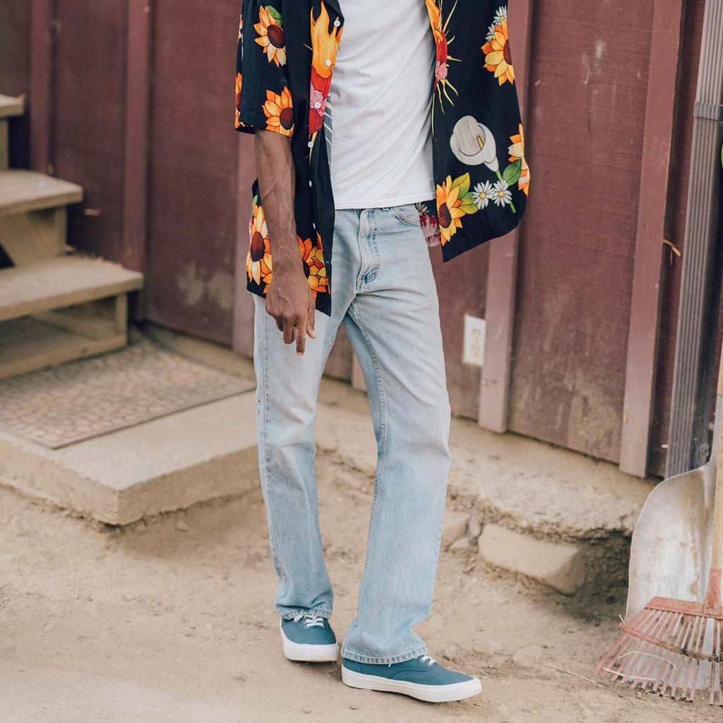 Men's Legend Sneaker in True Navy canvas, worn with light jeans and a floral shirt outside a wooden building
