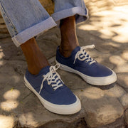 Men's Legend Sneaker in True Navy canvas, close-up worn with cuffed jeans on sandy rock
