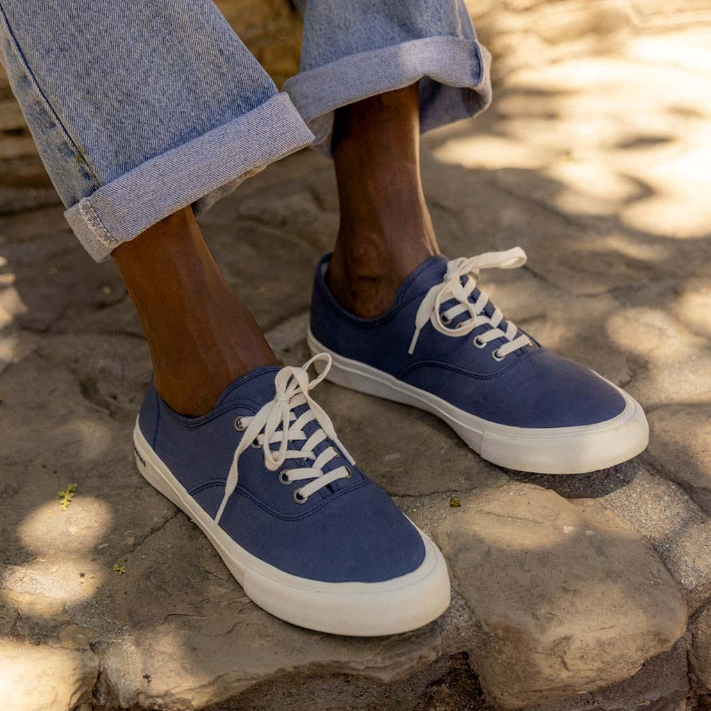 Men's Legend Sneaker in True Navy canvas, close-up worn with cuffed jeans on sandy rock