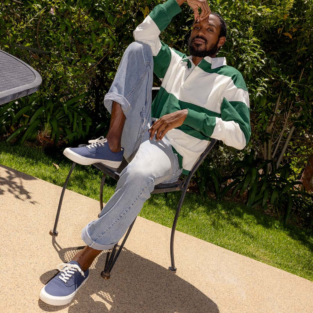 Men's Legend Sneaker in True Navy canvas, worn with jeans by a person seated in a patio chair