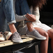 Men's Hermosa Sneaker in Tin Grey canvas, close-up worn by a person seated on a bench in cuffed jeans