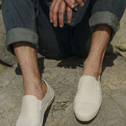 Men's Baja Slip On in Natural canvas, worn with cuffed jeans, close-up while seated outdoors