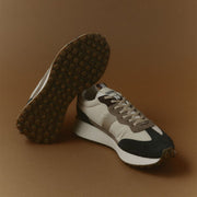 Men's Acorn Trainer sneaker in Black and Tan nylon and suede, pair shown on a tan studio background, one showing the outsole
