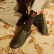 Men's Hawthorne Slip On in Black Olive leather, worn with khaki pants and dark socks on a patterned rug