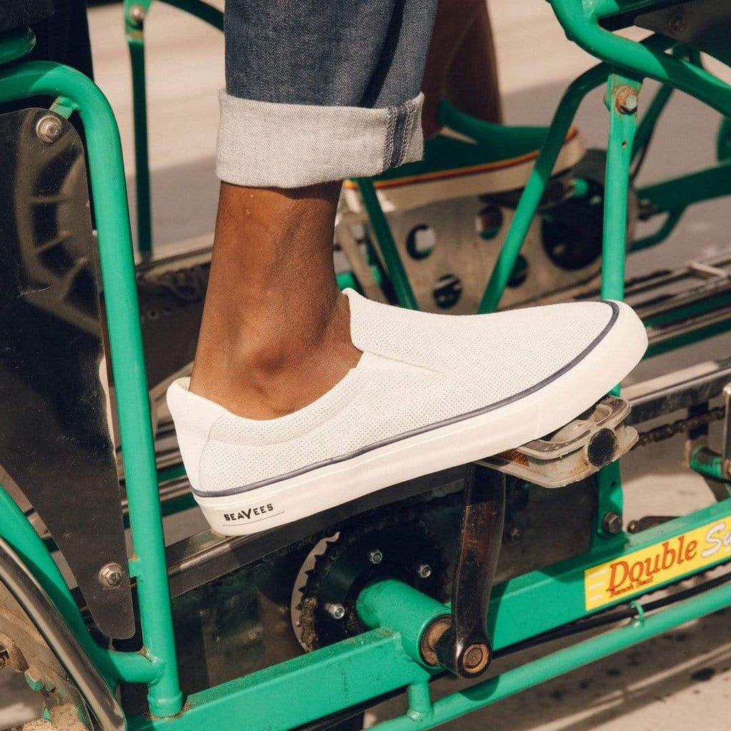 Men's Hawthorne Slip On in Ecru suede, close-up of a foot resting on a green pedal cart