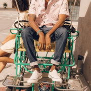 Men's Hawthorne Slip On in Ecru suede, worn with cuffed jeans by a person seated on a green pedal cart