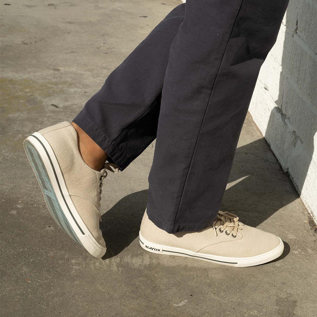 Men's Hermosa Sneaker in Natural canvas, close-up worn with dark pants on a sunny sidewalk