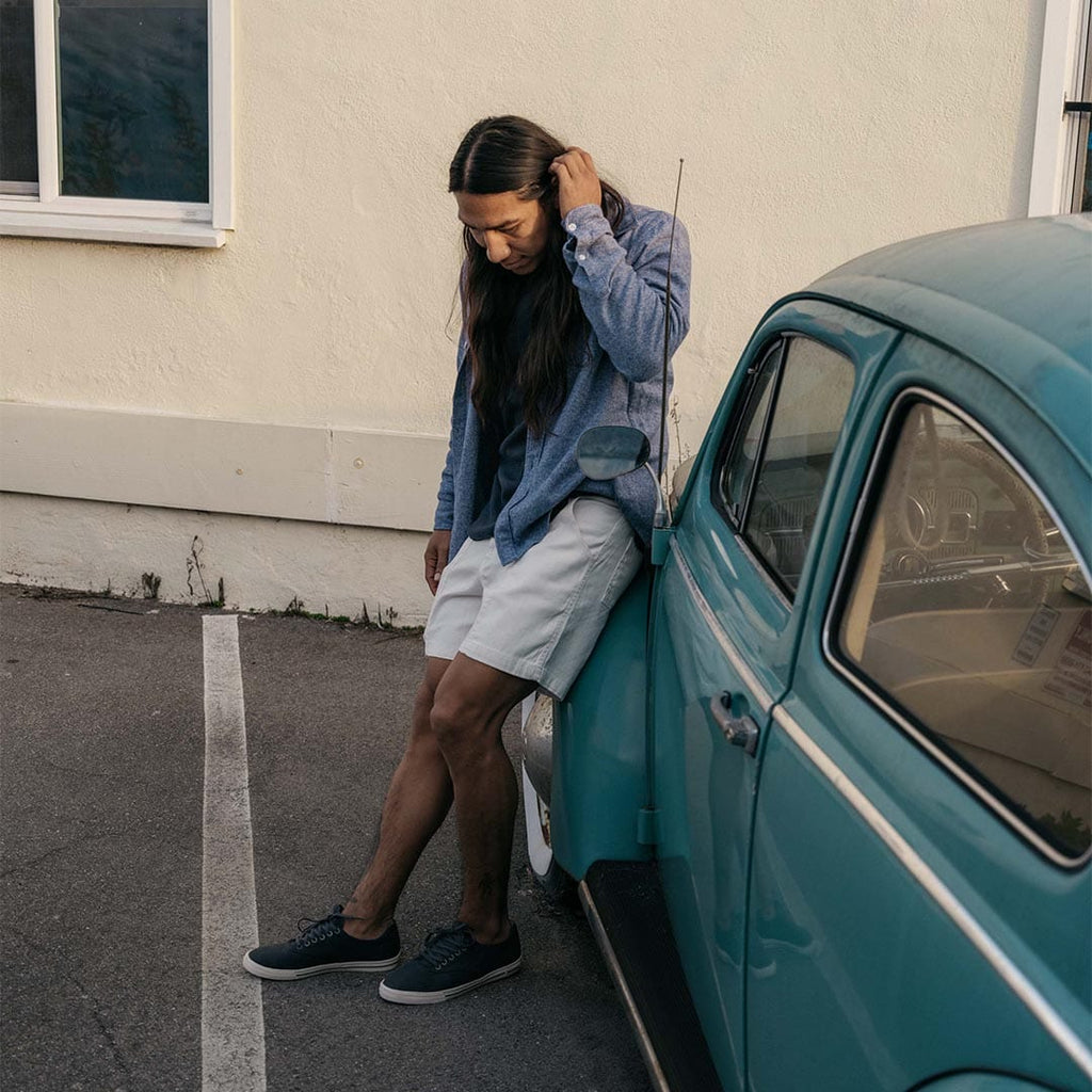 Men's Hermosa Sneaker in Slate Navy canvas, worn with shorts beside a teal vintage car