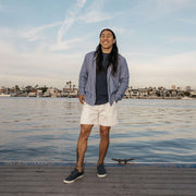 Men's Hermosa Sneaker in Slate Navy canvas, worn with white shorts by a person standing on a harbor dock