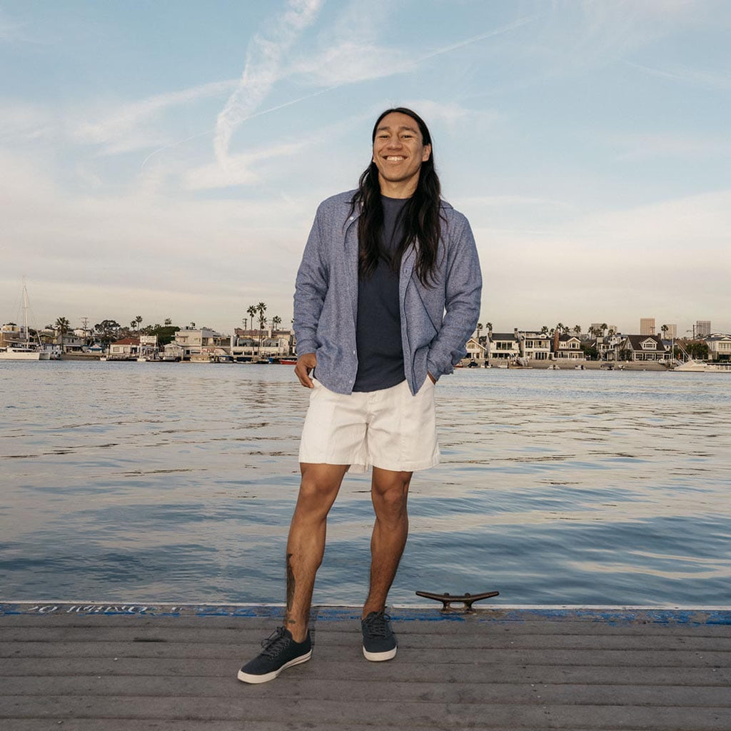 Men's Hermosa Sneaker in Slate Navy canvas, worn with white shorts by a person standing on a harbor dock