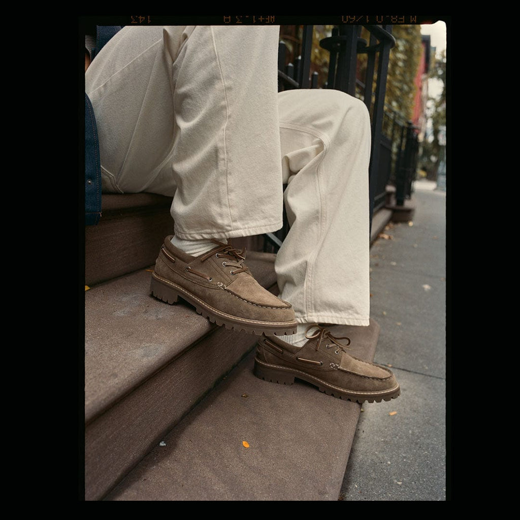 Men's Larkspur Lug Boat Shoe in Cement suede, worn with cream pants on city steps