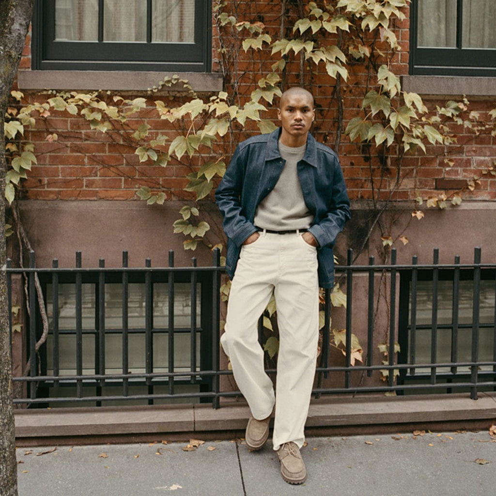 Men's Larkspur Lug Boat Shoe in Cement suede, worn by a person standing in front of a brick building in cream pants